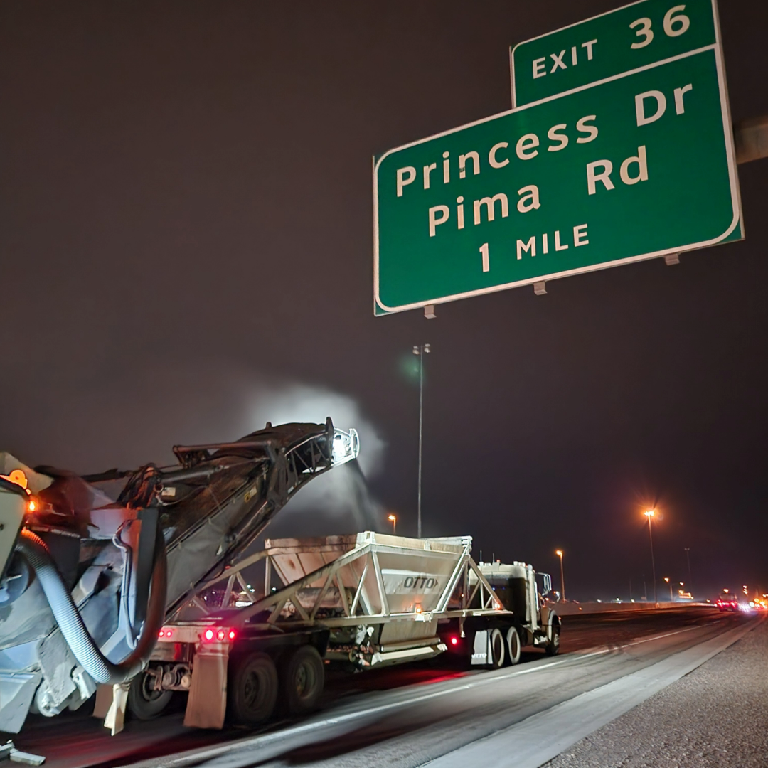 Heavy machinery removes the top layer of asphalt from a freeway at night.